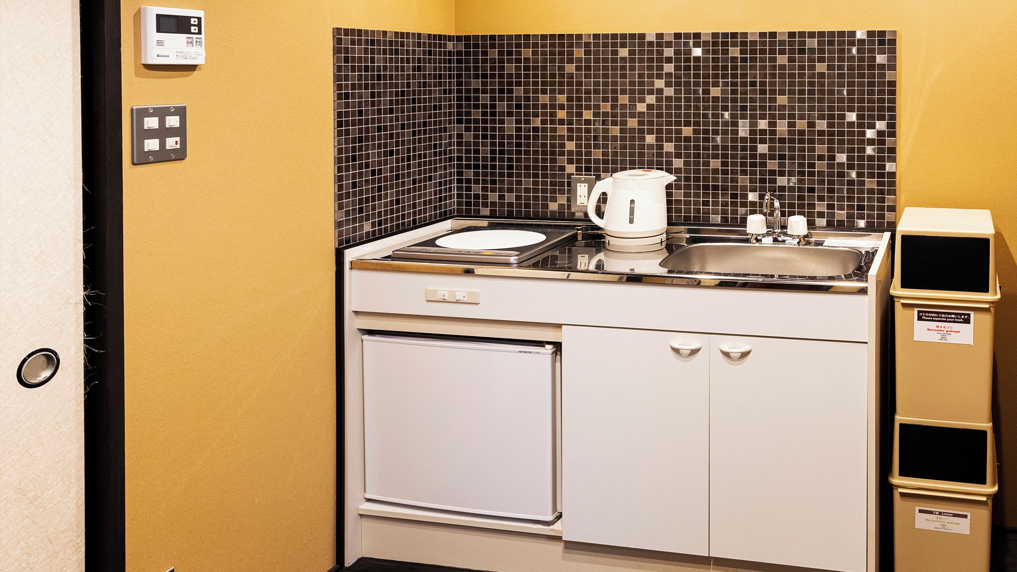Una piccola cucina componibile con macchina da caffè, lavello e cestino.