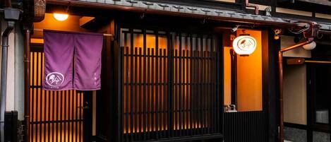 A traditional Japanese building with a wooden gate, a hanging purple banner, and a neon sign.