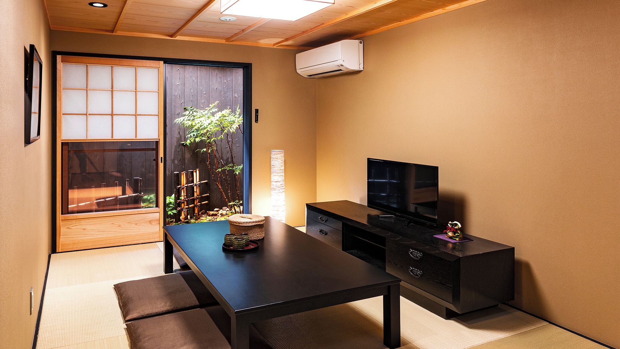 A room with a sliding door leading to a garden, a black TV stand, a woven basket, and a small decorative item.