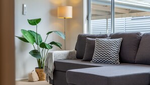 Una sala de estar moderna con un sofá gris, un cojín estampado, una lámpara de pie y una planta verde grande.