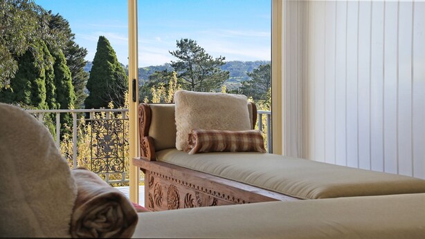 A balcony with a sofa and a bed, offering a view of trees and hills. - Southern Grace - the perfect Southern Highlands escape, spacious, stylish and serene (Bowral)