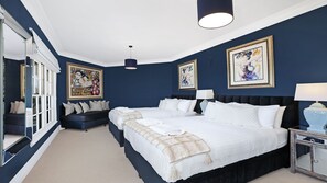 Un dormitorio amplio y azul oscuro con dos camas, ropa de cama blanca y obras de arte en las paredes.