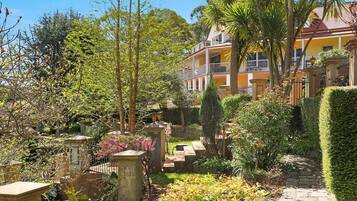 A garden with a stone pathway, a fountain, and a yellow building with a balcony.