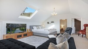 A bedroom with a skylight, a bed, a TV, a chandelier, and a view of a tree-lined path. - Southern Grace - the perfect Southern Highlands escape, spacious, stylish and serene (Bowral)