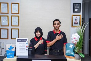 Ein Empfangsschalter mit gerahmten Zertifikaten an der Wand, ein Schild für Denz Express und ein Schild als zertifizierter Hotelpartner von Traveloka.