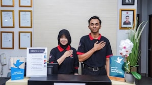 Een receptiebalie met ingelijste certificaten aan de muur, een bord met Denz Express en een bord dat aangeeft dat het een erkend Traveloka hotelpartner is.
