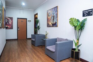 Ein Empfangsbereich mit einer Holztür mit der Aufschrift 701, zwei grauen Sofas, einem großen Gemälde und einem Schild, das den Weg zum Café weist.