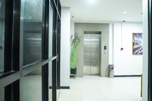 Eine helle, moderne Lobby mit Glastür, Blumentopf, Aufzug und einem gerahmten Bild an der Wand.
