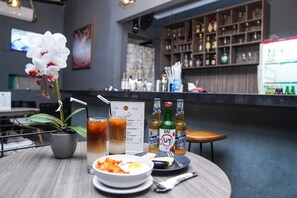 Ein Tisch mit einer Topforchidee, einer Schüssel mit Essen und zwei Bierflaschen, im Hintergrund eine Speisekarte und eine Bar.