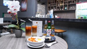 Een tafel met een potorkidee, een schaal eten en twee bierflesjes, met een menukaart en een bar op de achtergrond.