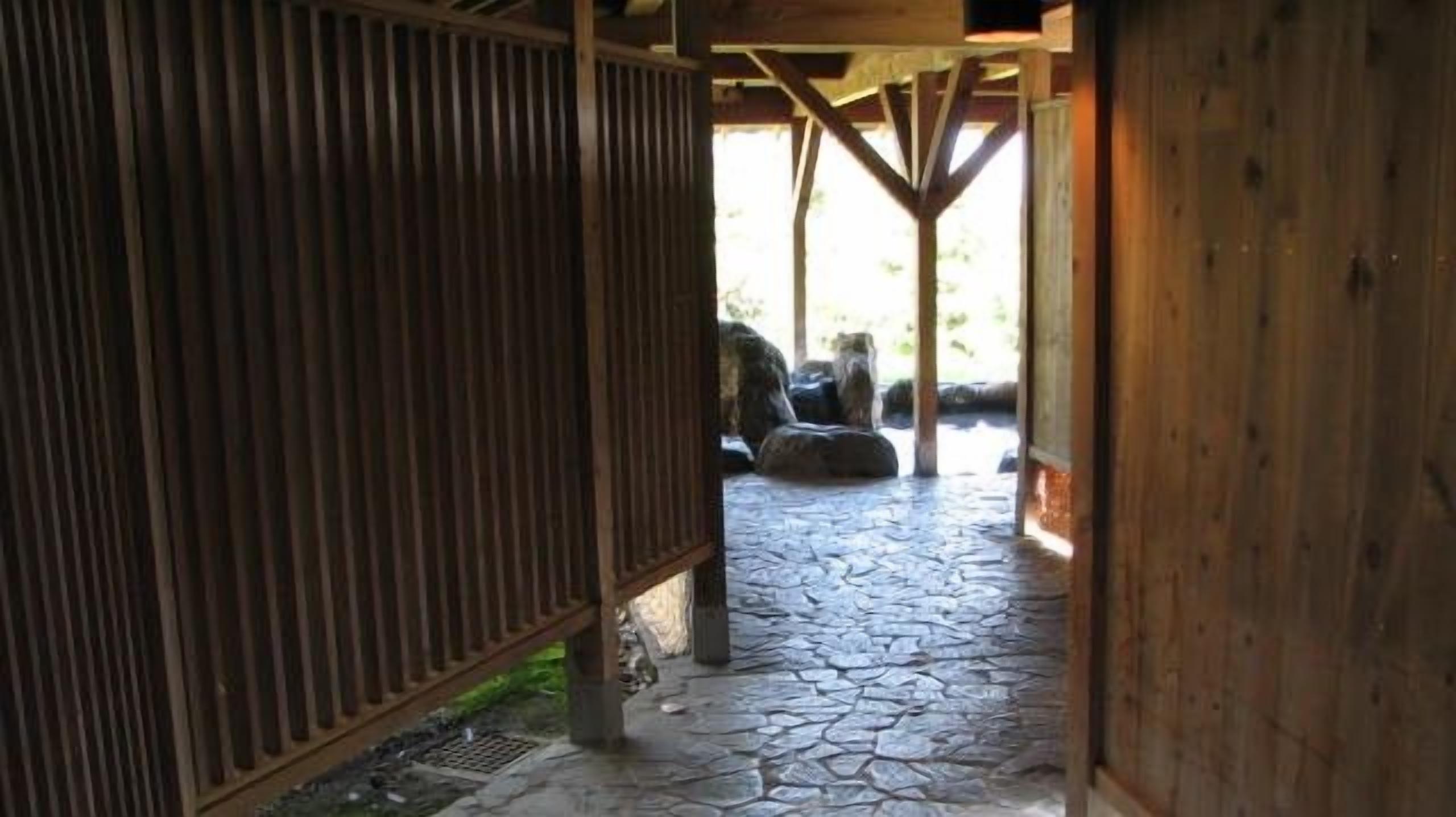 Un pasillo con suelo de piedra que conduce a un espacio exterior con estructuras de madera.
