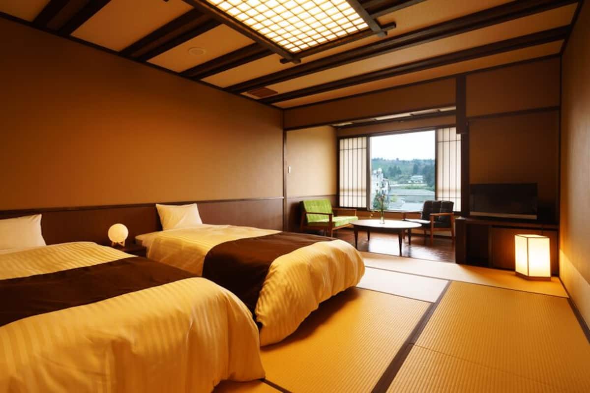 A hotel room with two beds, a small table, a chair, a television, and a view of the outside.