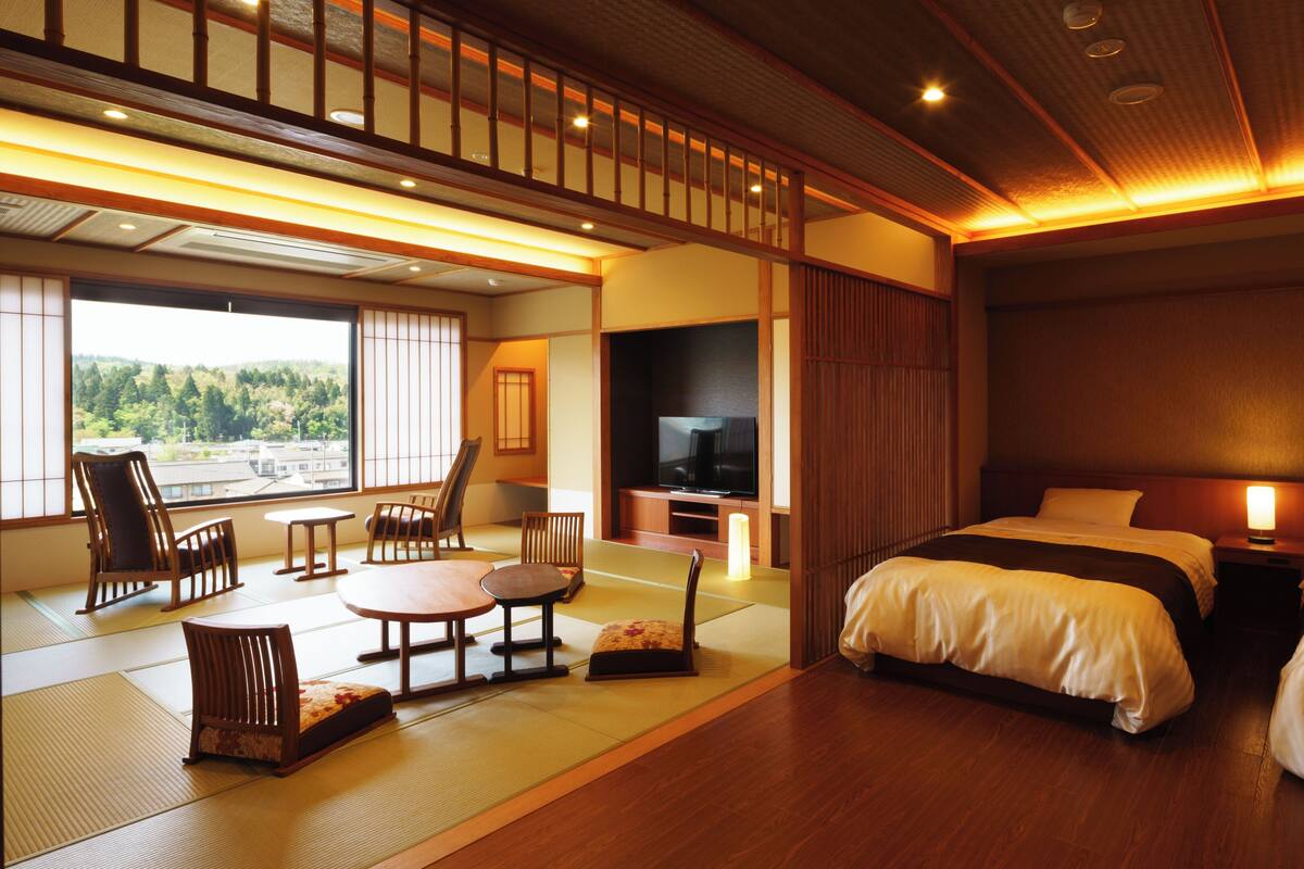 A hotel room with tatami flooring, a television, a sofa, a bed, and a view of the outdoors.