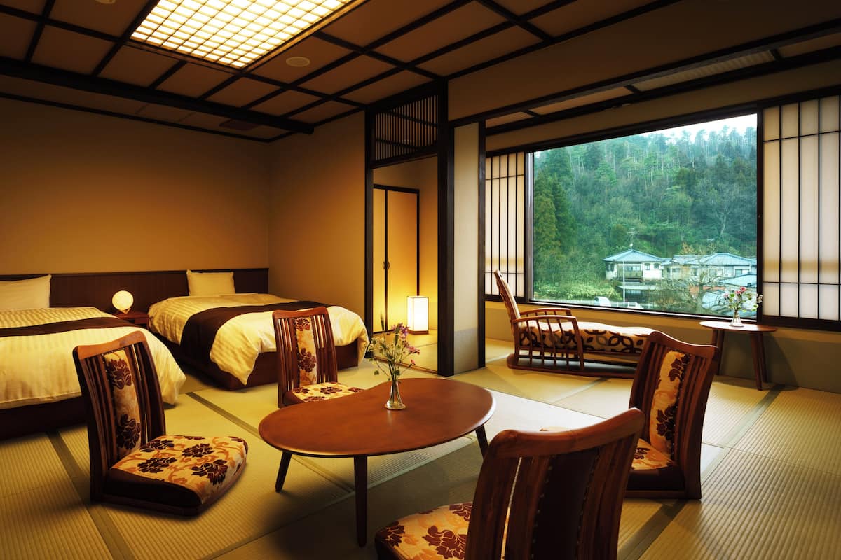 A traditional Japanese-style hotel room with tatami flooring, two beds, a small table, and chairs.