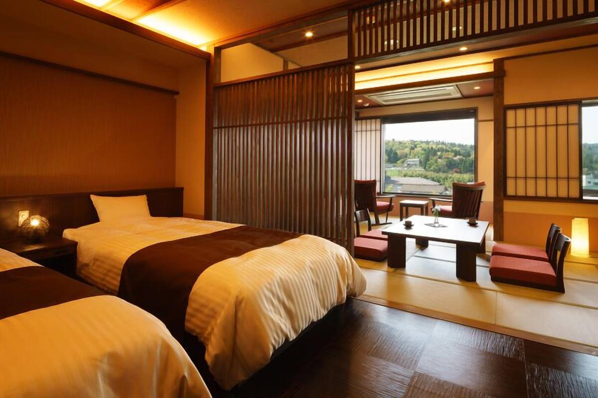 A hotel room with two beds, a sitting area with a table and chairs, and a view of the outdoors.