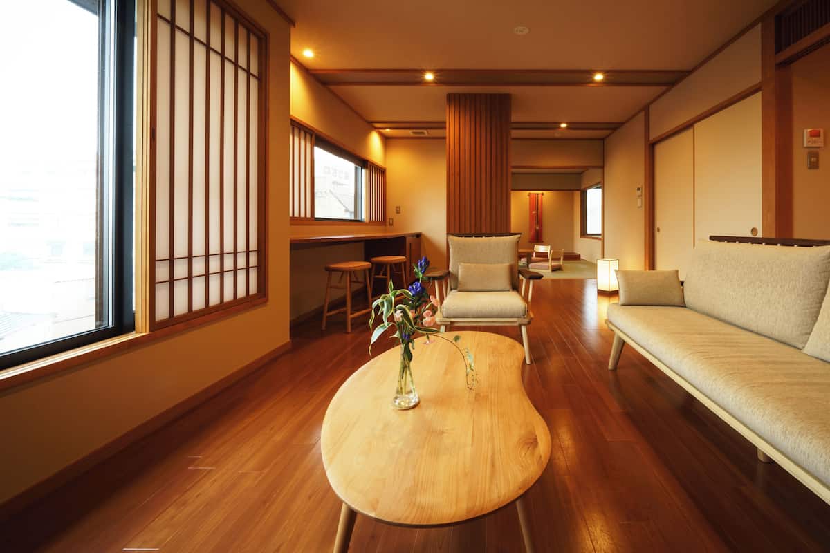 A traditional Japanese-style room with tatami flooring, a low wooden table with a vase, a sofa, and a chair.