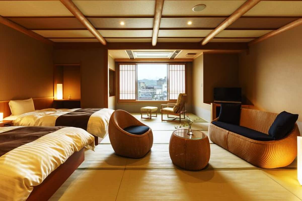 A hotel room with two beds, a sofa, a chair, a small table, and a TV.