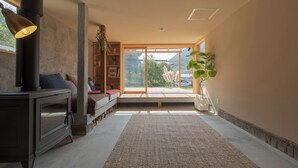 A modern living room with a fireplace, a sofa, a bookshelf, and a large window with a view of greenery. - La Toile (Mitoyo)
