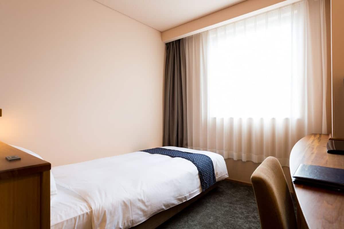 Una habitación de hotel con una cama individual, un escritorio, una silla y una ventana con cortinas.