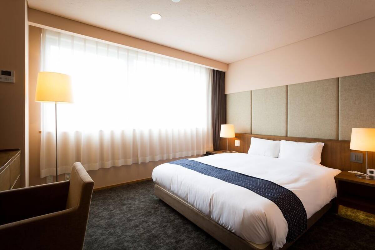 A hotel room with a large bed, two bedside lamps, a desk, and a chair.