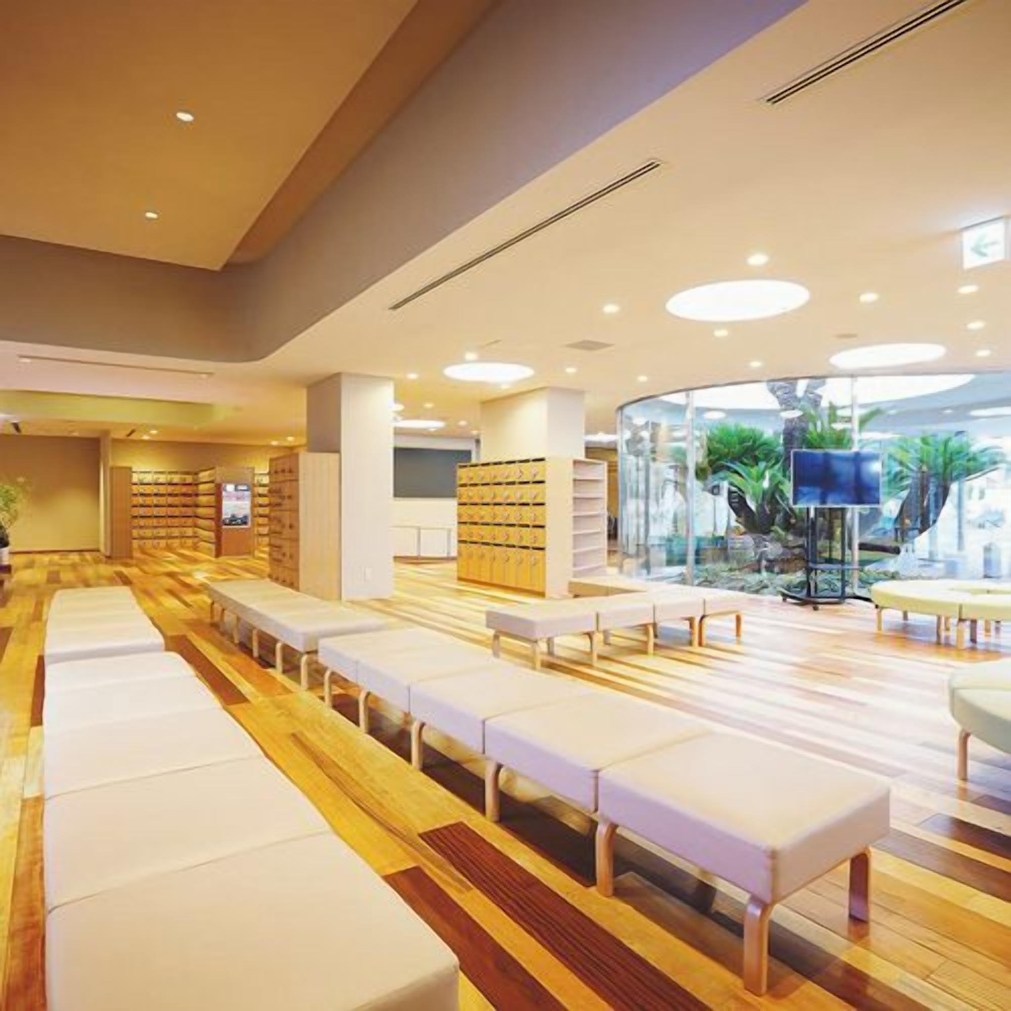A spacious indoor area with rows of white benches and bookshelves, a curved glass wall, and a ceiling with recessed lighting.