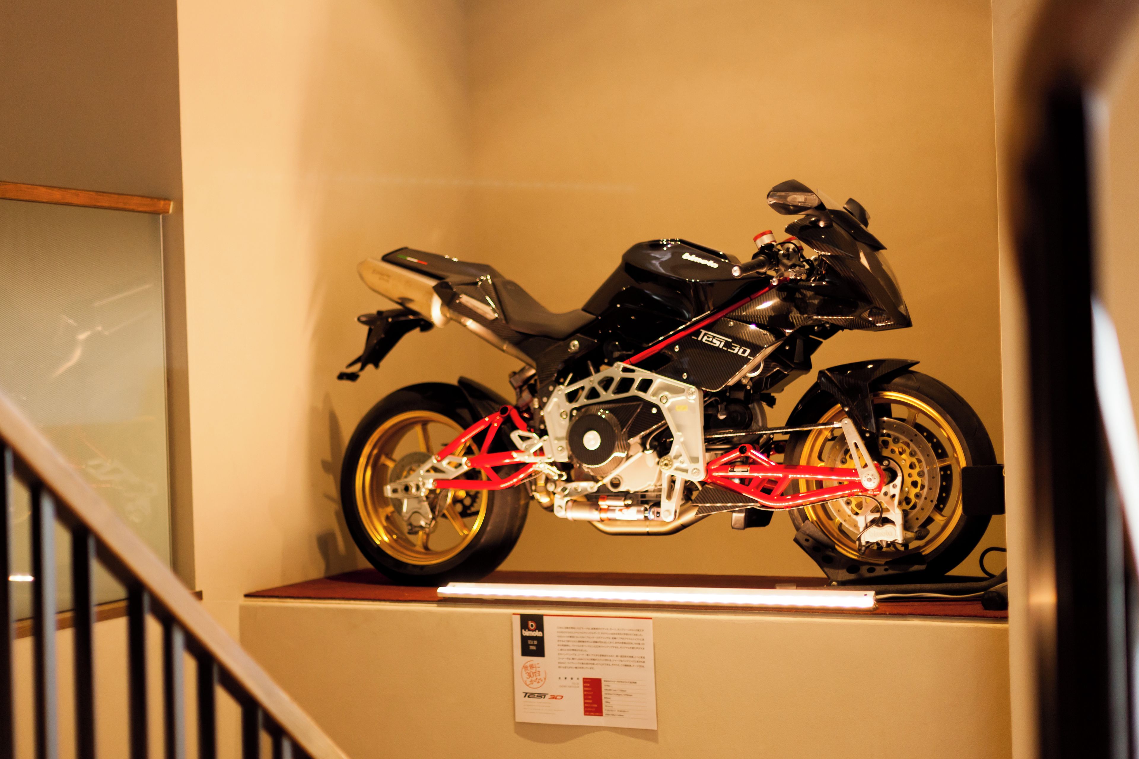 Une moto exposée sur un présentoir fixé au mur, dans une pièce dotée d’un escalier.
