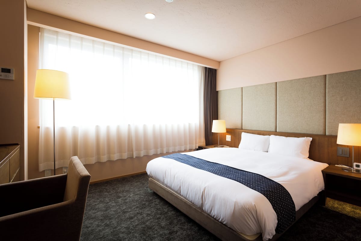 A hotel room with a large bed, two bedside lamps, a desk, and a chair.