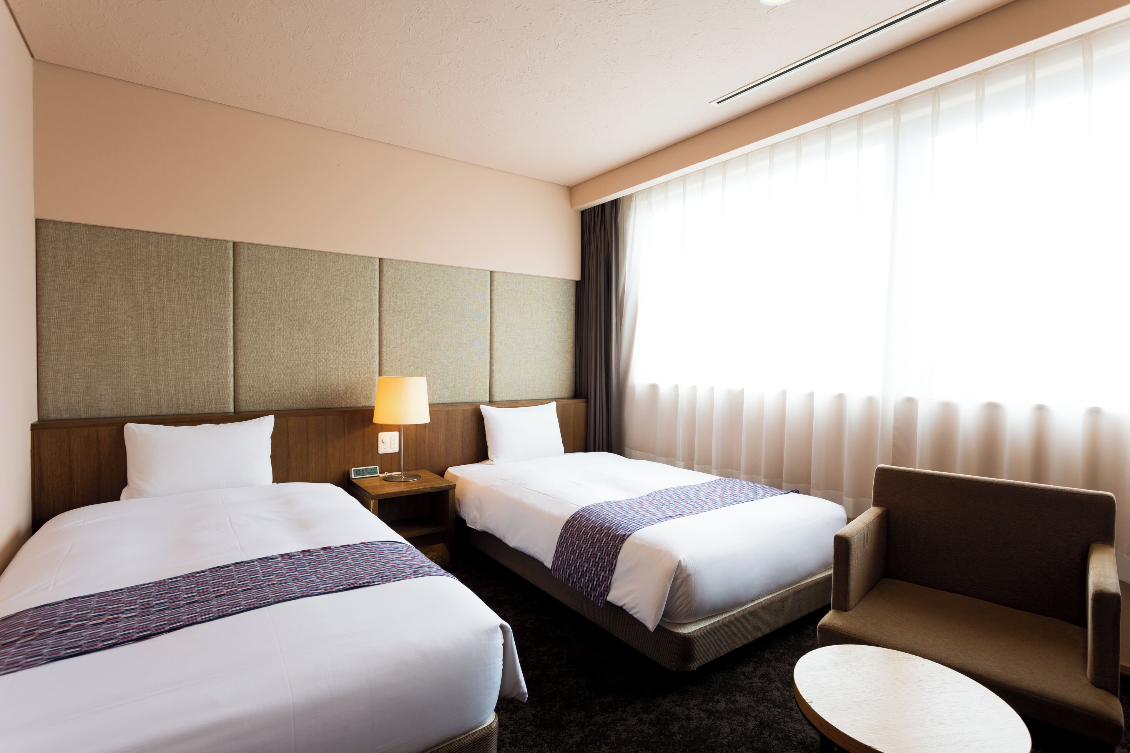 Habitació d'hotel amb dos llits, una petita taula de nit, una làmpada, una cadira i una taula rodona.