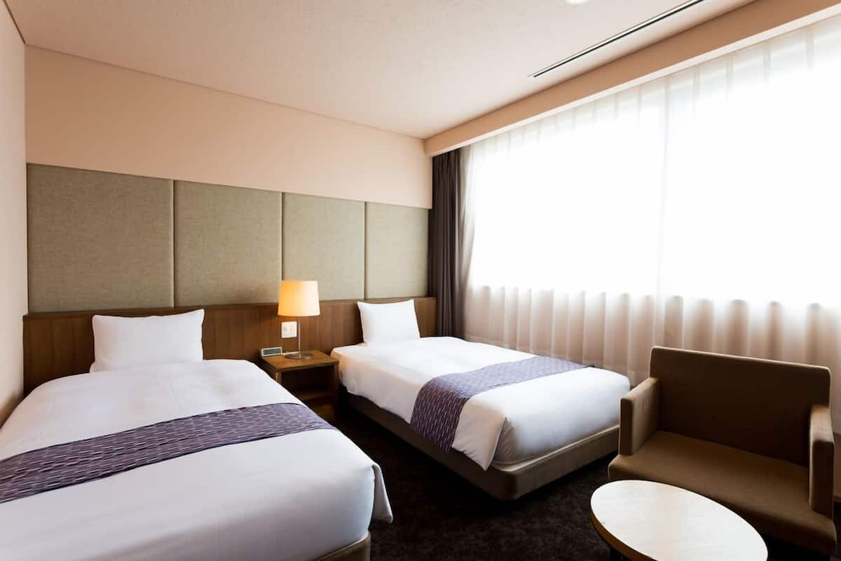 A hotel room with two beds, a nightstand, a lamp, a chair, and a round table.