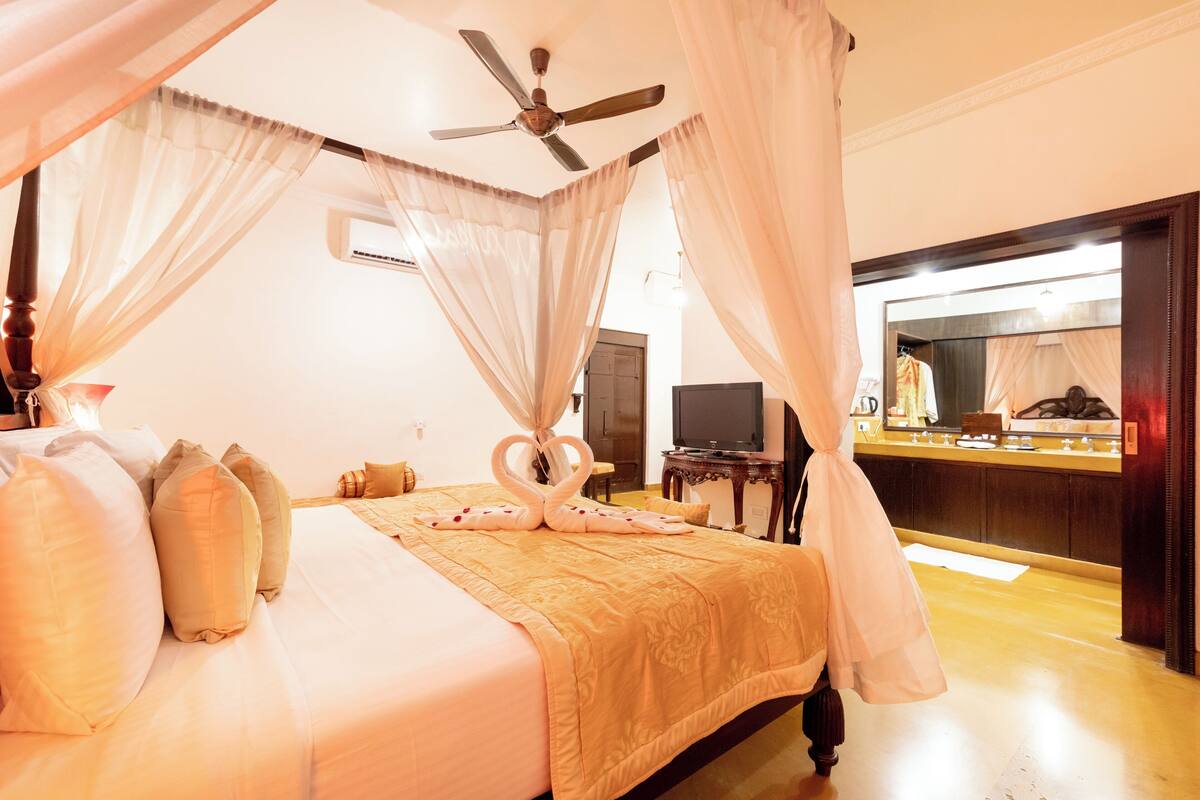 A four-poster bed with a canopy, a ceiling fan, and a minibar.
