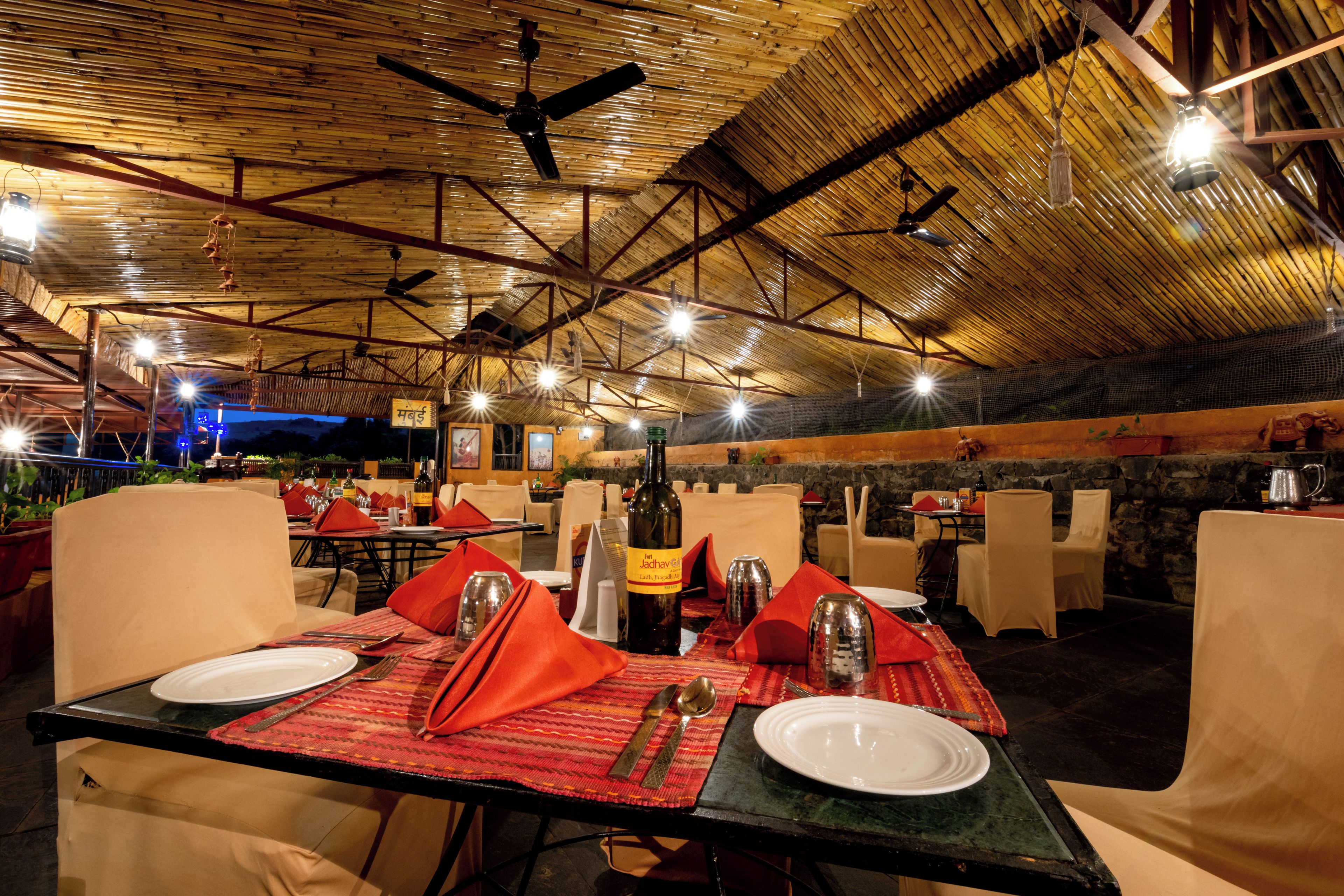 Un restaurant en plein air avec des tables disposées pour le service, doté d’un plafond en bois rustique et d’un éclairage d’ambiance.