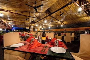 An outdoor restaurant with tables set for dining, featuring a rustic wooden ceiling and ambient lighting. - Fort Jadhavgadh (Sasvad)