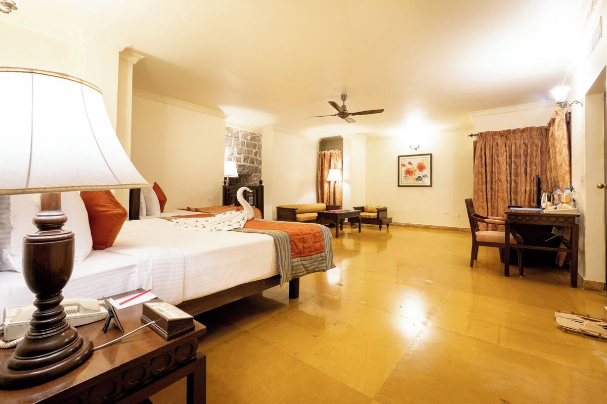 A hotel room with a bed, bedside table, lamp, and a desk with a chair.