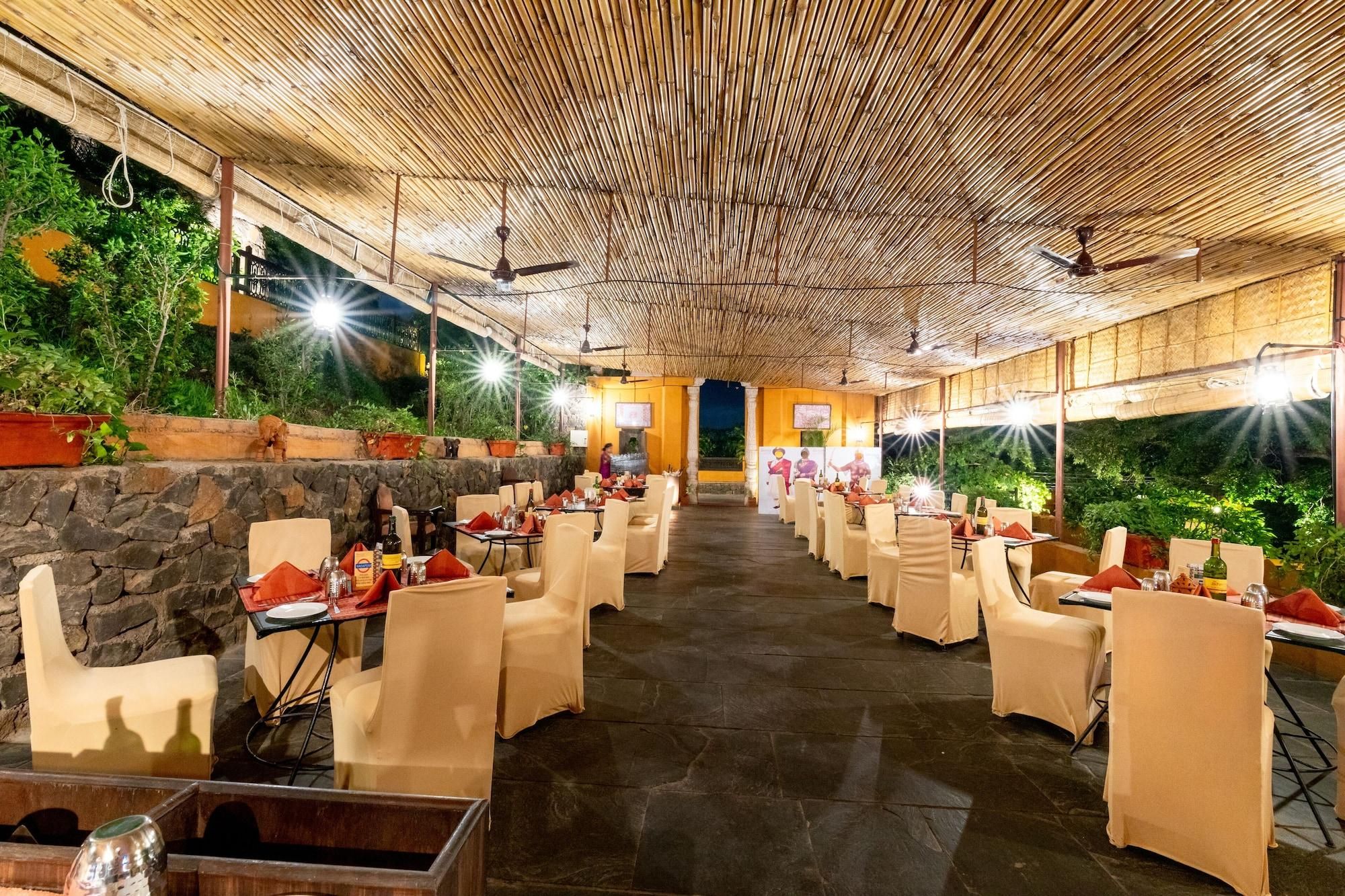 A restaurant with a bamboo ceiling, stone walls, and outdoor seating. Tables are covered with beige tablecloths and have red napkins.