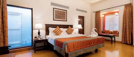 A hotel room with a large bed, two bedside tables with lamps, a window with curtains, a door, and a wall-mounted artwork.