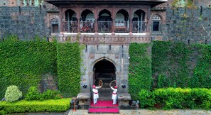 A historic building with a stone facade, arched windows, and a red carpet leading to the entrance. - Fort Jadhavgadh (Sasvad)