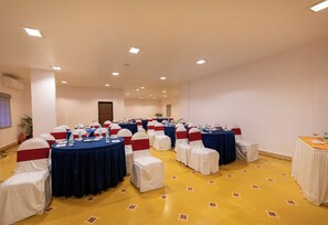Un salón de conferencias con mesas redondas, sillas blancas con cintas rojas y alfombra de diseño amarillo.