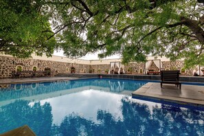 En swimmingpool med väggar och bänkar av sten, omgiven av träd.