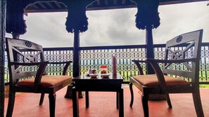 Un balcón con dos sillas de madera y una mesa, con vistas a un jardín y un cielo nublado.