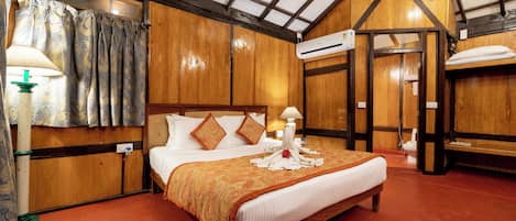 A wooden-paneled bedroom with a large bed, two bedside lamps, and an air conditioning unit.