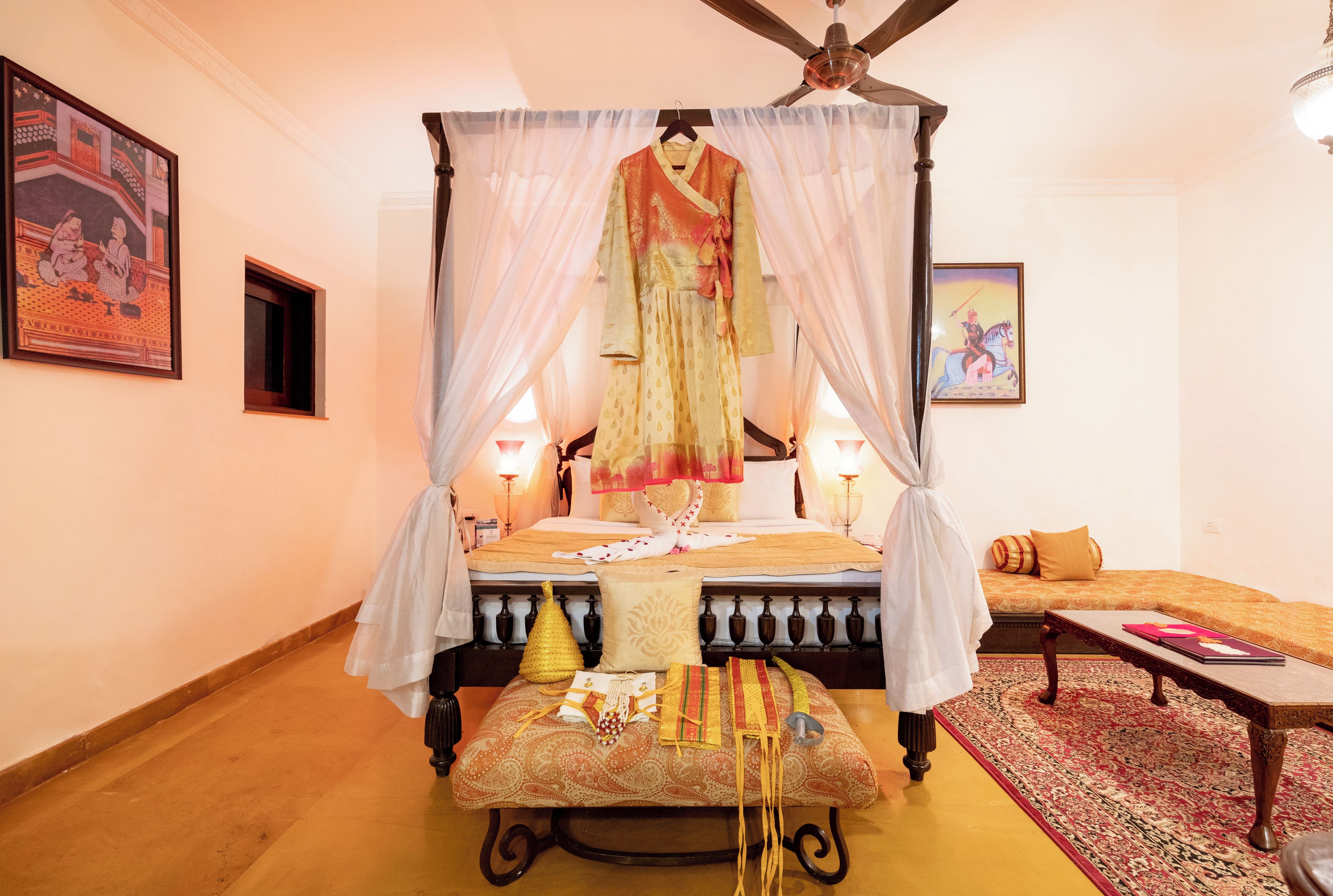 A bedroom with a four-poster bed, a bedside table, a small sofa, and a decorative rug.