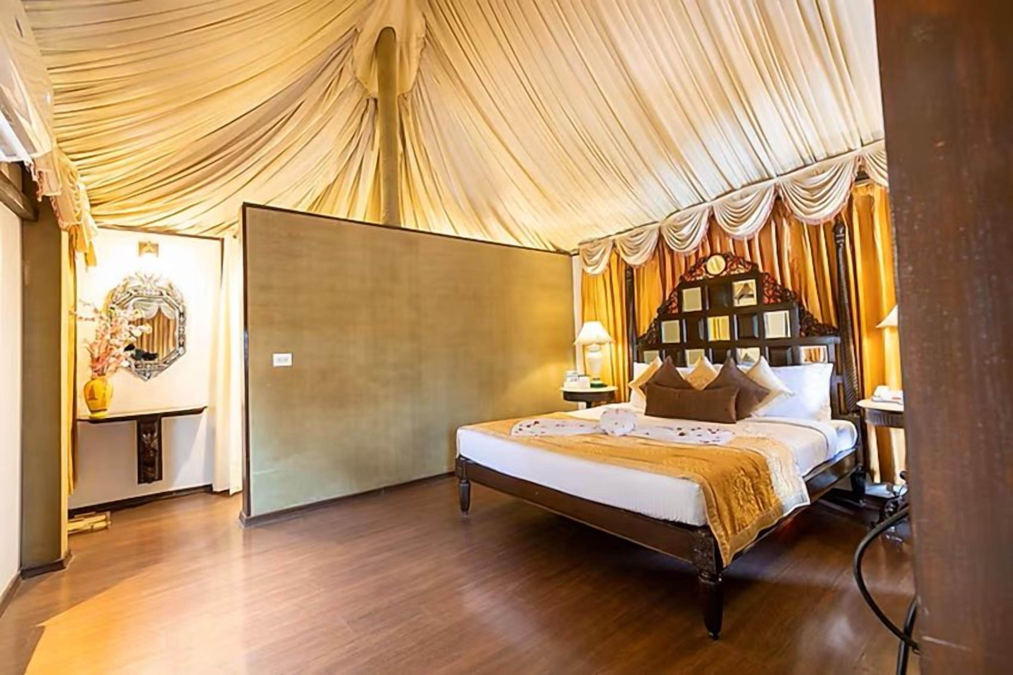 Een slaapkamer met een groot bed, een nachtkastje, een klok aan de muur en een decoratieve spiegel.