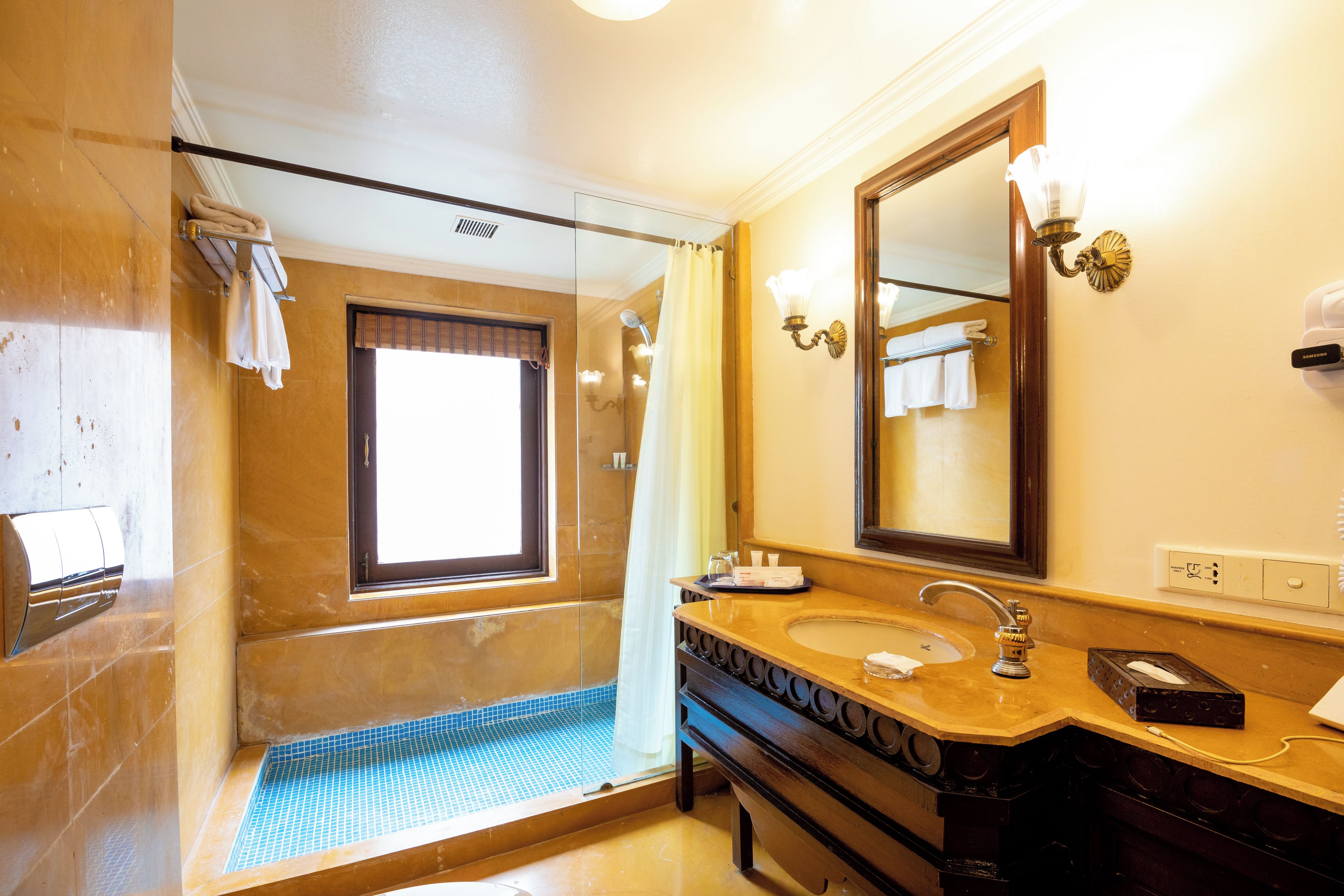 Un baño con un espejo grande, un lavamanos, una ducha con puerta de cristal y un perchero para toallas.