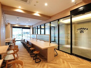 A modern interior with long wooden tables and chairs, a herringbone floor pattern, and large windows. - Henn na Hotel Premier Nagoya Fushimi Ekimae (Nagoya)