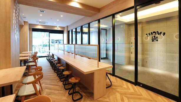 Un café moderno con muebles de madera, una barra larga y ventanas amplias.