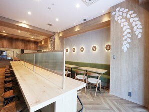 A modern restaurant interior with a long wooden counter, multiple seating areas, and a decorative wall with circular patterns. - Henn Na Hotel Express Nagoya Fushimi Ekimae (Nagoya)