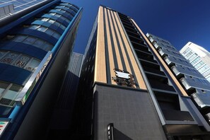A modern high-rise building with a prominent vertical wooden panel design and a logo at the top. - Henn na Hotel Premier Nagoya Fushimi Ekimae (Nagoya)