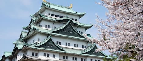 A traditional multi-tiered building with green roofs and white walls, surrounded by cherry blossoms.