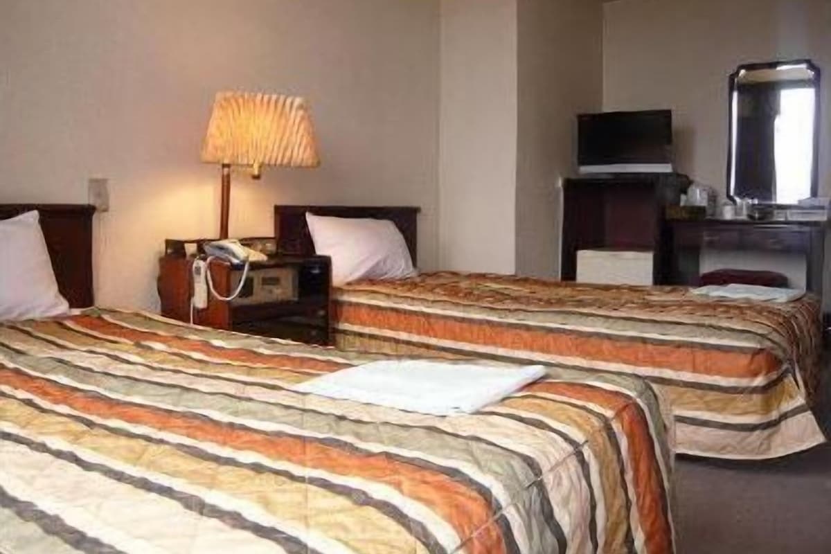 A hotel room with two beds, a desk with a lamp, a television, and a mirror.