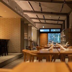 A modern interior with a brick wall, wooden tables, and a large window providing a view of the outdoors. - Arita Huis (Arita)